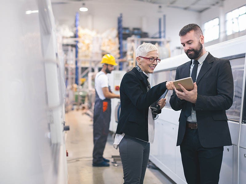 Diverse professionals review information on a tablet while facility professional in a hard hat works on machinery