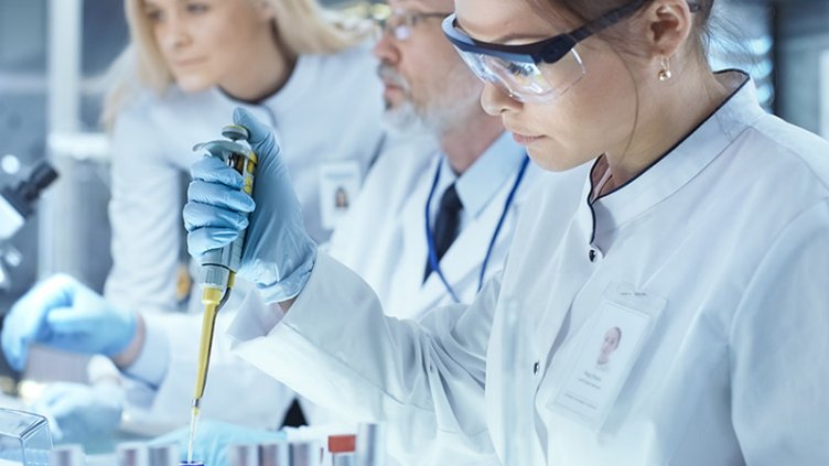 Team of Research Scientists Working With Personal Computer, Analysing Test Trial New Generation Drug Data and Using Micropipette for Filling Test Tubes. They Work in a Modern Laboratory Center