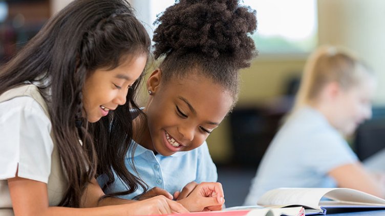 School girls smiling and reading book during science class