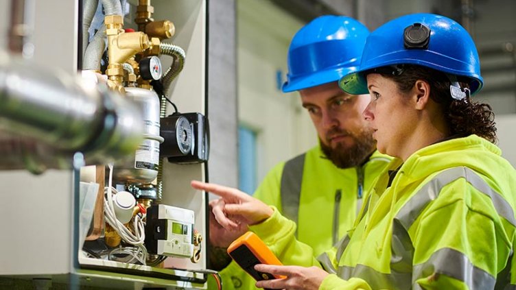 Female facility management leader points to equipment, training a male FM professional in an industrial environment